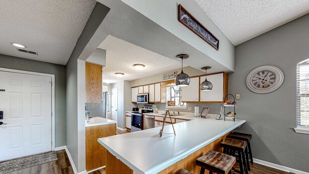 A kitchen with a large island, wooden stools, a clock, and a sign above the island. - Inviting 2BR Condo - HOT TUB - Family Pool (Branson)
