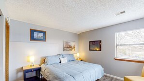 A bedroom with a bed, two bedside tables, a chair, and three framed pictures on the wall. - Rustic 2BR Condo - POOL & GOLF - Pet Friendly (Branson)