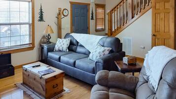Ein Wohnzimmer mit Ledersofa, Holzschrank, Lampe und einer Treppe.