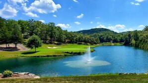 Un campo de golf sereno con un estanque, árboles y un cielo despejado.