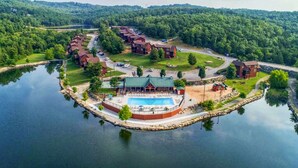 Un complejo turístico junto al lago con piscina, cabañas para huéspedes y un muelle.