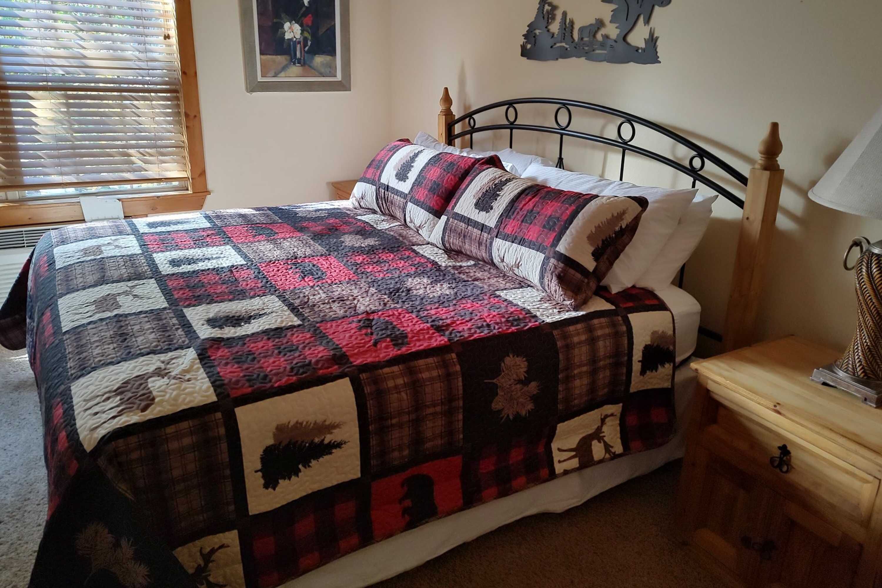 Ein Bett mit einer Steppdecke, ein Nachttisch aus Holz, eine Lampe und ein Bild an der Wand.