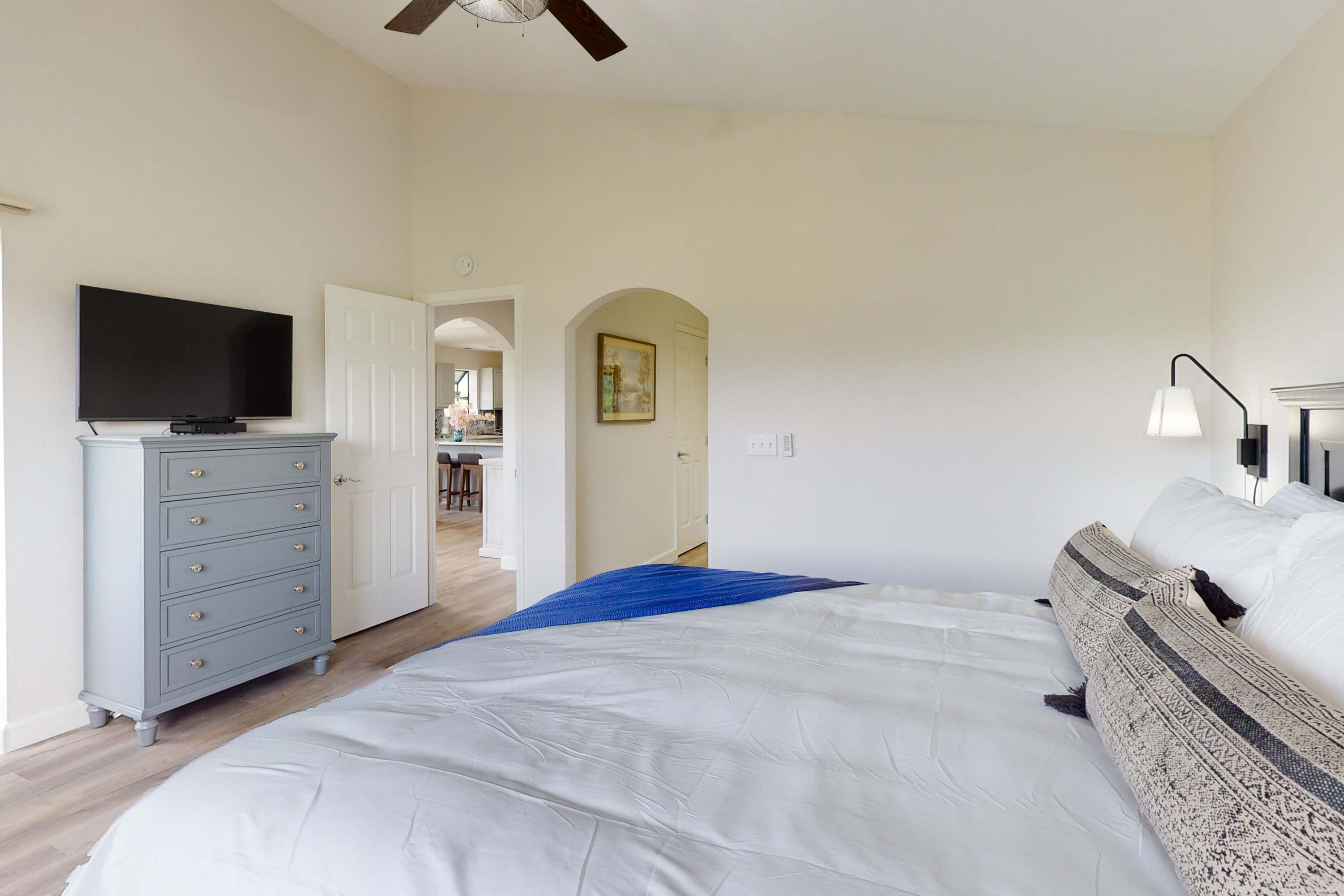 A bedroom with a bed, a dresser, a television, and a hallway leading to another room.