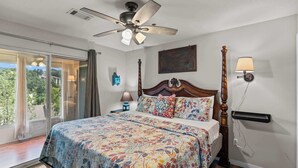 A bedroom with a bed, a ceiling fan, a nightstand, a lamp, a window with curtains, and a view of greenery outside. - Rustic 2BR Condo - FARMHOUSE STYLE - Fall Creek (Branson)