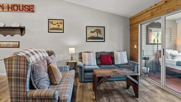 A cozy living room with a plaid sofa, a blue sofa with patterned cushions, a wooden coffee table, and a glass door leading to a balcony. - Rustic 2BR Condo - FARMHOUSE STYLE - Fall Creek (Branson)
