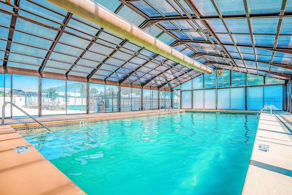 Una piscina interior con agua azul cristalina, techo metálico y vistas al exterior.