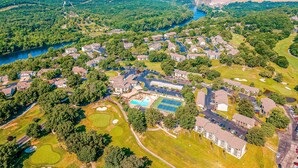 Ett flygbildsfoto av ett bostadsområde med hus, en swimmingpool, tennisbanor och en flod.