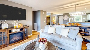 A modern living room with a fireplace, grey sofa, dining area, and kitchen. - Bright 2BR Condo - JETTED TUB & POOL - Branson (Branson)