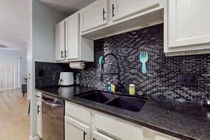 Eine Küche mit weißen Schränken, einer schwarzen Spritzschutzwand, einer Edelstahl-Spüle und einem Wasserhahn.