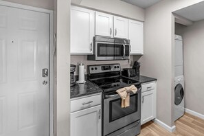 A compact kitchen with a stainless steel microwave, stove, and oven, a washing machine, and white cabinetry. - Serene 2BR Condo - POND VIEW - Pointe Royale (Branson)