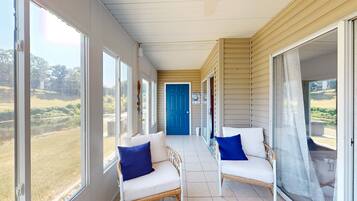 A covered porch with two wicker chairs, a blue door, and large windows overlooking a landscape.