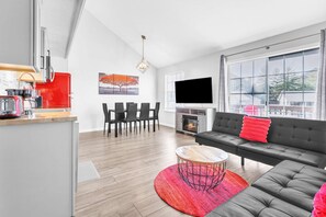A modern living room with a sofa, a coffee table, a TV, a fireplace, and a dining area with chairs. - Charming 2BR Condo - Loft - POND VIEWS Branson (Branson)