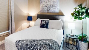 A neatly made bed with a zebra-patterned throw, a wall-mounted painting of a tree, a bedside lamp, and a potted plant. - Bright 2BR Condo - Seasonal POOL - Branson (Branson)