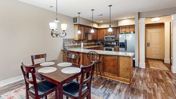A kitchen with wooden cabinets, a granite countertop, and a dining area with a wooden table and chairs. - Bright 2BR Condo - Seasonal POOL - Branson (Branson)