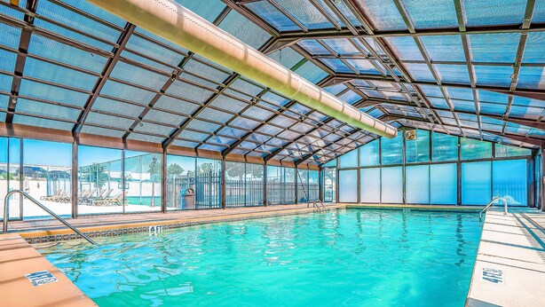 Piscina interior com água azul cristalina, estrutura coberta e vista para o exterior.