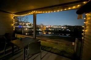 A covered outdoor area with a table and chairs, a view of a cityscape, and string lights. - Cozy 2BR - POND VIEWS - Pool & Golf Discount (Branson)