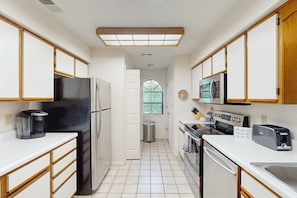 A kitchen with white cabinets, a black refrigerator, a microwave, a toaster, and a window with a view of greenery. - Golf Course 2BR # Heated Pool # Branson Condo (Branson)