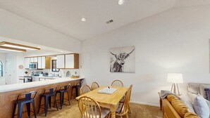 Una cucina moderna con angolo bar, un tavolo da pranzo con sedie e un soggiorno con divano e lampada.