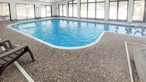 Una piscina interna con acqua cristallina, pavimento effetto pietra e ampie finestre.