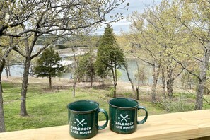 Deux tasses vertes ornées de l’inscription « Table Rock Lake House », posées sur une rambarde en bois donnant sur un lac et des arbres.