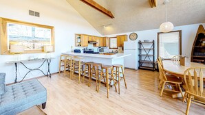 A kitchen with wooden cabinets, a central island with stools, a dining table with chairs, and a large window with blinds. - Lakefront 4BR Cabin # POOL TABLE # Lake Views (Reeds Spring)