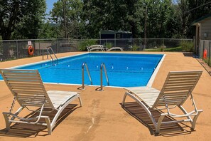 Une piscine rectangulaire avec deux échelles en métal, entourée d’une terrasse en sable.