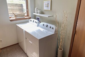 Une buanderie équipée d’un lave-linge et d’un sèche-linge à chargement frontal, d’une fenêtre avec un porte-linge et d’une étagère ornée d’objets décoratifs.
