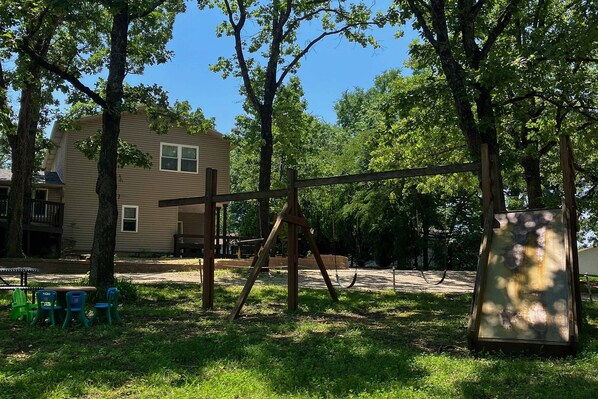 Un parc avec une aire de jeux comprenant des balançoires, des tables de pique-nique et un bâtiment en arrière-plan.