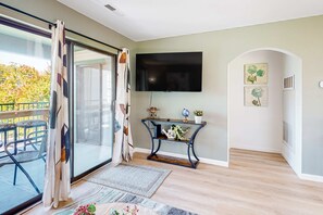 A modern living room with a sliding glass door, a flat-screen TV, a console table with decorative items, and a view of the outdoors. - Peaceful 2BR Condo - GOLF COURSE - Pool in Branson (Branson)