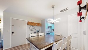 A dining area with a wooden table and white chairs, a kitchen in the background, and a ceiling light fixture. - Bright 3BR Condo - MOUNTAIN VIEWS - Community Pool (Branson)