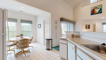 A modern kitchen with white cabinetry, a stainless steel sink, and a dining area with a table and chairs.
