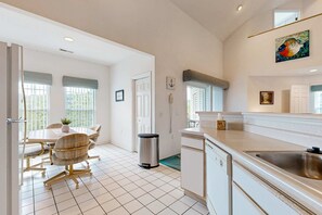 A modern kitchen with white cabinetry, a stainless steel sink, and a dining area with a table and chairs. - LAKEFRONT -3BRcondo-Resort amenities-Peaceful (Kimberling City)