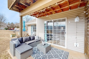 Eine überdachte Terrasse mit einem Rattansofa, einem Glastisch und einem gemusterten Teppich.