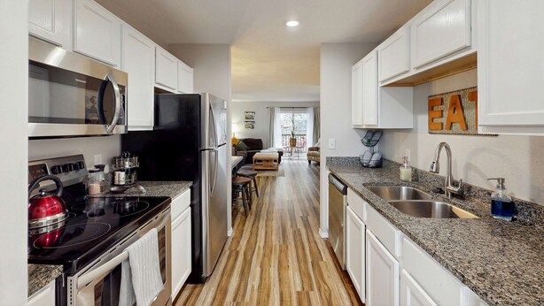 A modern kitchen with white cabinetry, stainless steel appliances, a granite countertop, and a wooden floor. - Serene 3BR Condo - MOUNTAIN VIEW - Community Pool (Branson)