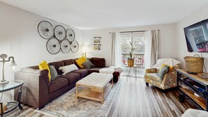 A living room with a brown sofa, ottoman, and patterned armchair, a coffee table, a lamp, and wall art. - Serene 3BR Condo - MOUNTAIN VIEW - Community Pool (Branson)
