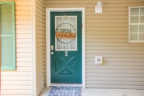 A teal front door with a 'stay awhile' sign, a number '2' above it, and a 'welcome' mat at the entrance. - Comfy 2BR Condo - FIREPLACE - Sleeps 6 Branson (Branson)