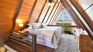 Een gezellige slaapkamer op zolder met een schuine hemel, een bed met een gestreept dekbed, een nachtkastje met een lamp, en uitzicht door een raam.