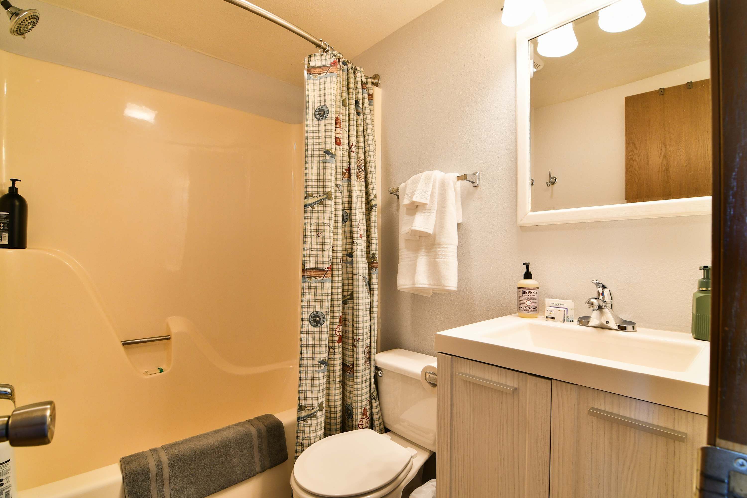 A bathroom with a shower, toilet, sink, and mirror.