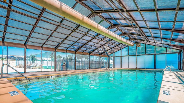 Ein Hallenbad mit klarem, blauem Wasser, einem Metalldach und Blick ins Freie.