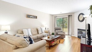Ein Wohnzimmer mit Sofa, Sessel, Couchtisch, Lampe und Kamin.