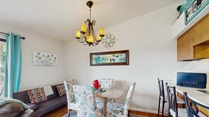 A living room with a sofa, dining table, chairs, a chandelier, and artwork on the walls. - Serene 1BR Retreat - GOLF VIEW - Pools & Fireplace (Branson)