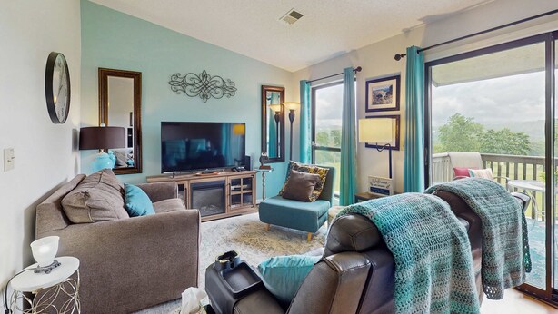 A living room with a TV, sofa, and a view of the outdoors. - Serene 1BR Retreat - GOLF VIEW - Pools & Fireplace (Branson)