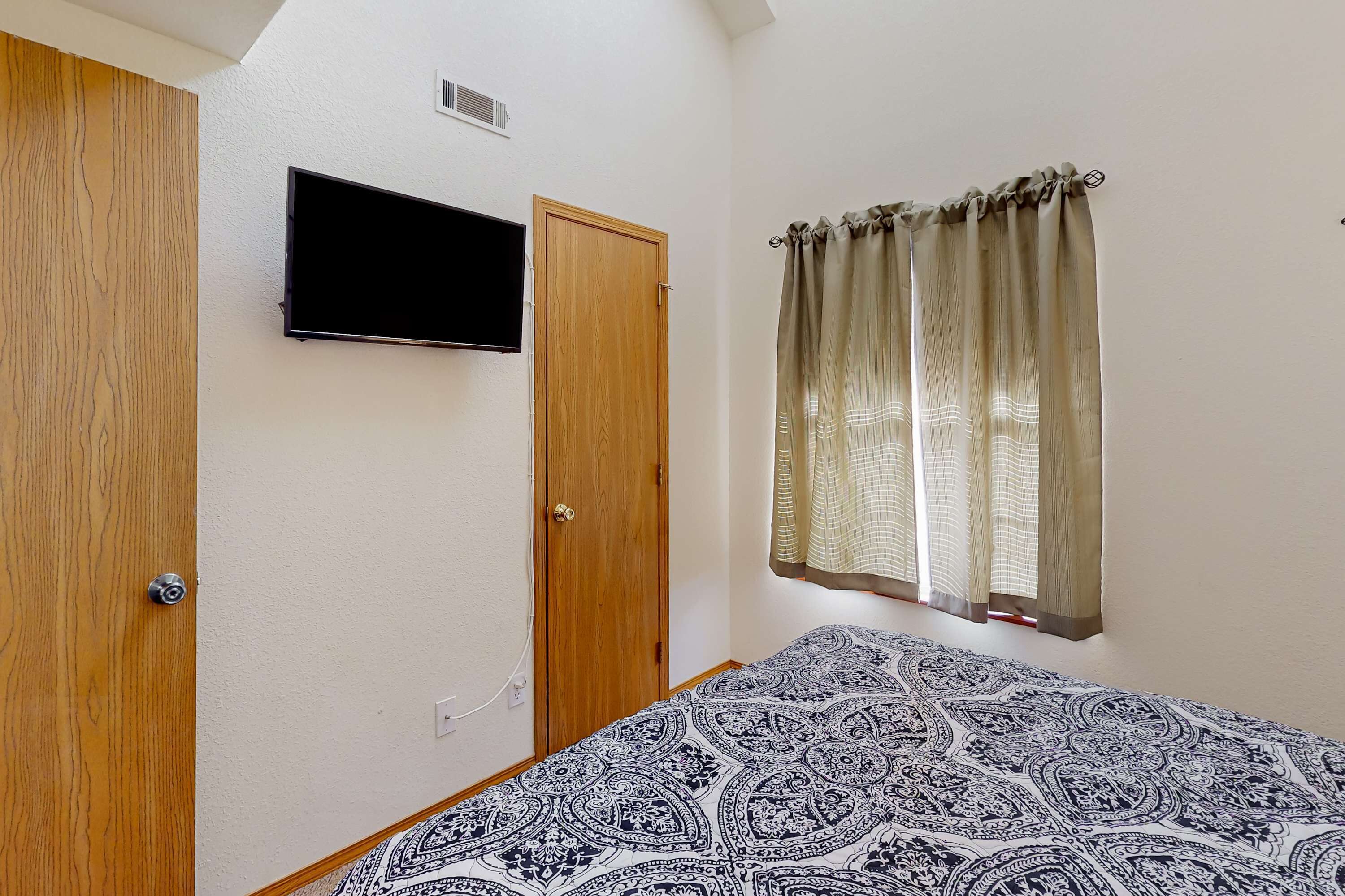 A bedroom with a bed, a television mounted on the wall, a wooden door, and a window with curtains.