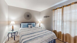 Een slaapkamer met een bed, twee nachtkastjes met lampen, een decoratief object aan de muur en een raam met gordijnen.