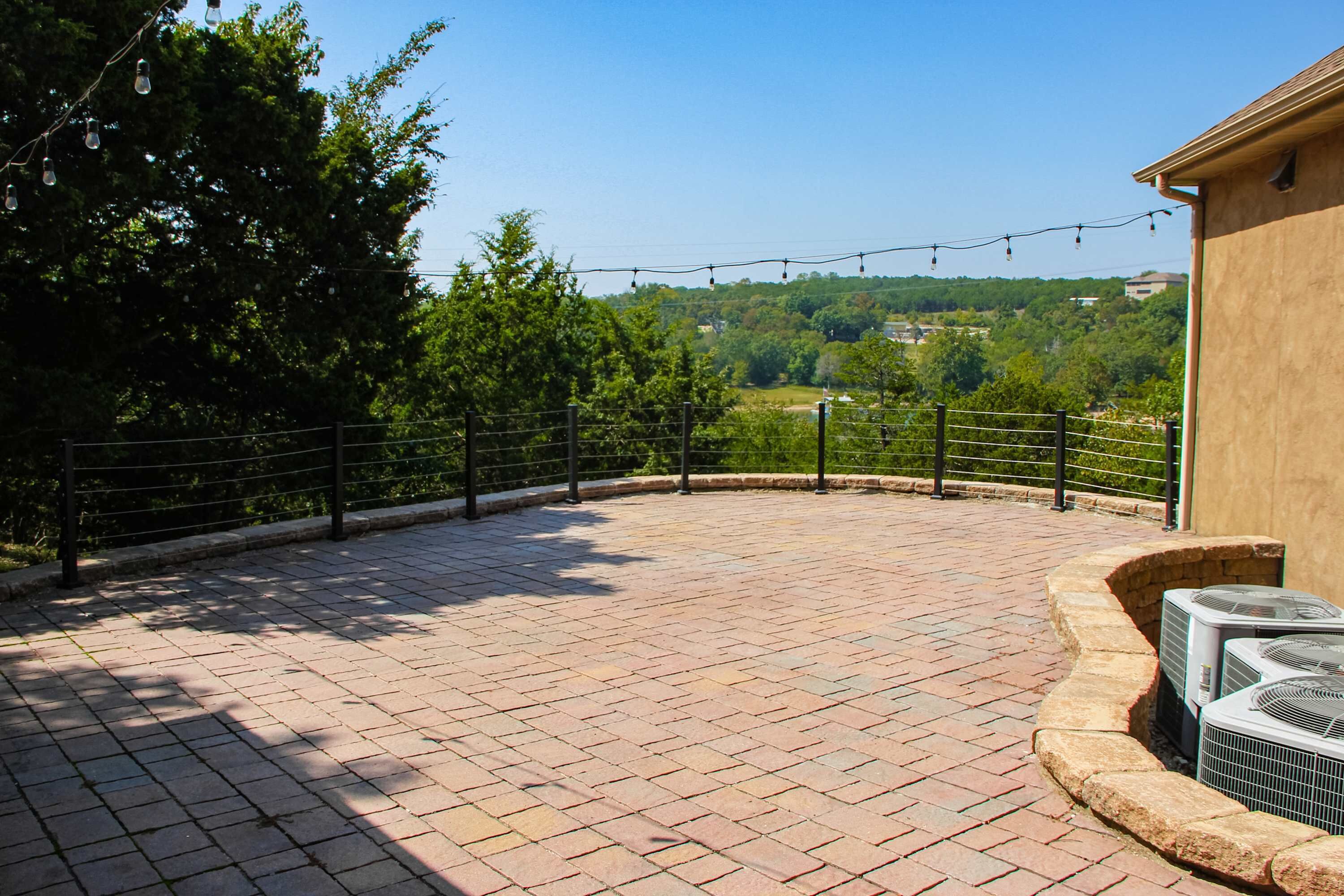 Eine gepflasterte Terrasse mit Freiluftklimaanlagen, einem Metallgeländer und Blick auf eine grüne Landschaft.