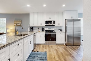 A modern kitchen with white cabinets, stainless steel appliances, and a granite countertop. - Classic 2BR Condo - SUN PORCH - Golf Course & Pool (Branson)