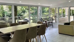 Una habitación amplia con una mesa grande y sillas, ventanas panorámicas con vista a la vegetación y un diseño de techo moderno.