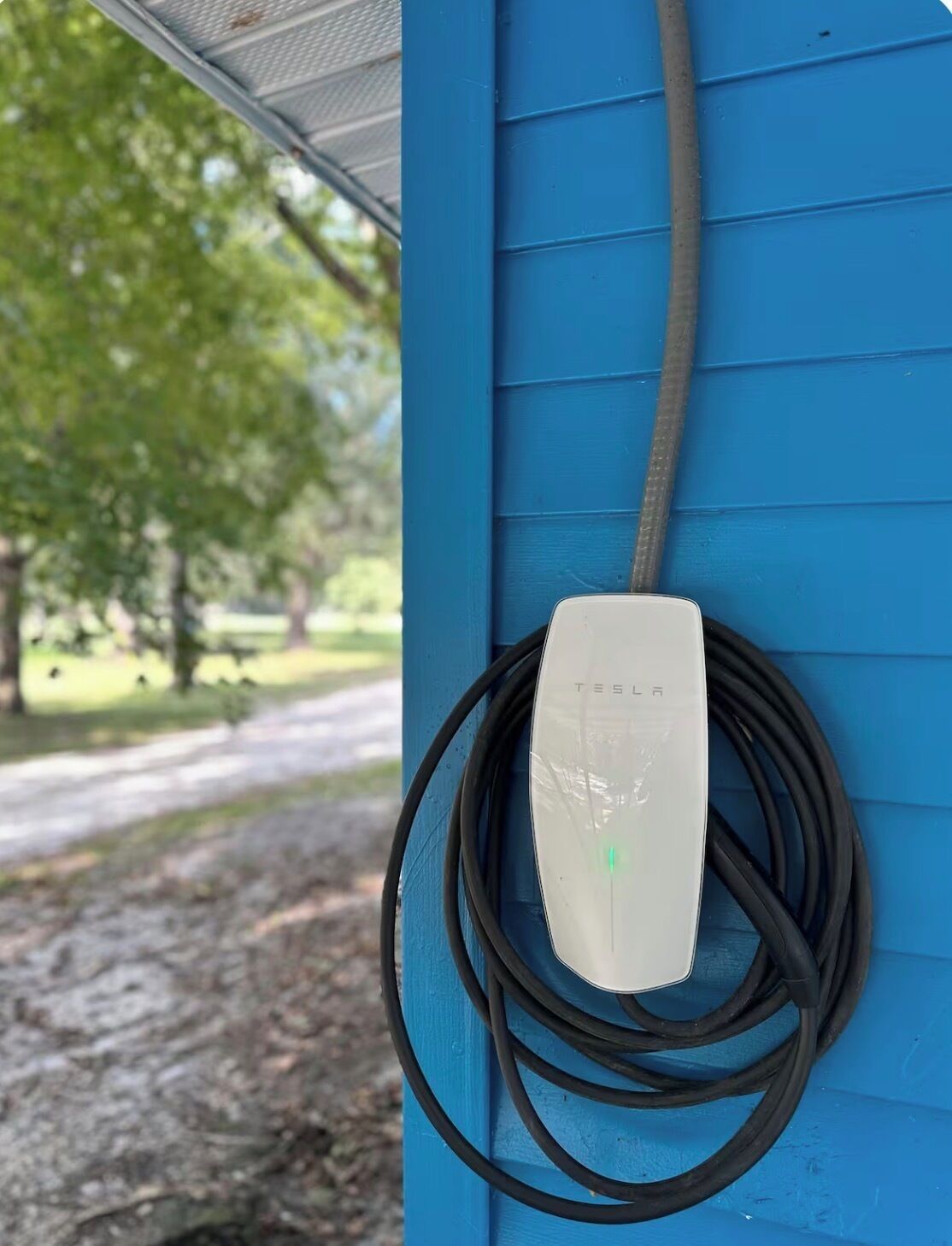 Une borne de recharge Tesla fixée à un mur bleu, avec un câble branché.