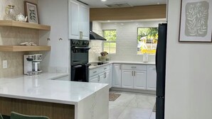 Una cocina moderna con armarios blancos, una isla de mármol y un refrigerador negro.