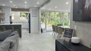 Una cocina moderna con iluminación empotrada, un comedor con mesa y sillas, y un amplio ventanal con vistas a zonas verdes.